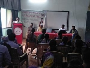 a white kitten with brown and black spots sitting with its paws slightly outstretched.